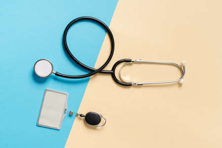 Overhead view of a stethoscope with a badge lying sideways on a beige and blue background in the...