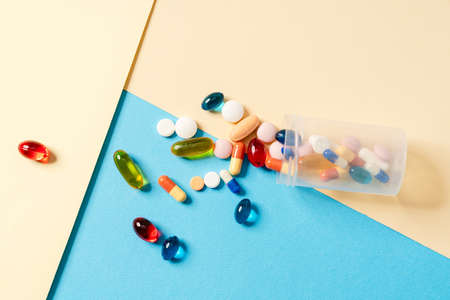 Close-up view of a scattered multicolored pills in a transparent jar lying on a colored background...