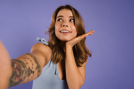 Young white woman smiling and taking selfie photo isolated over purple backgroundの写真素材
