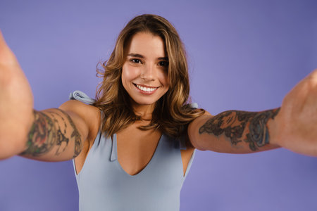 Young white woman smiling and taking selfie photo isolated over purple backgroundの写真素材