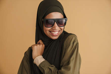 Black muslim woman in hijab smiling and looking at camera isolated over beige background