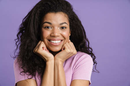 Close up of a happy young african woman in casual clothes standing over violet background, looking at camera, smilingの写真素材