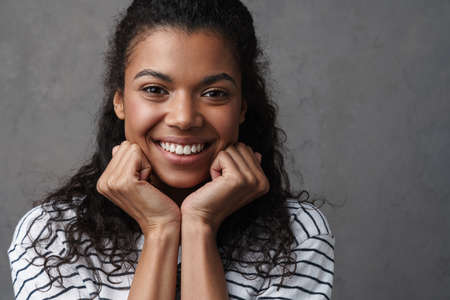 Happy young african woman in casual wear standing over gray background, looking at camera