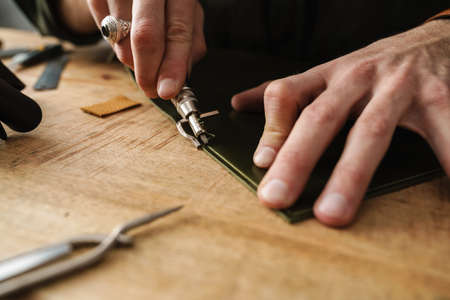White craftsman working with leather at wooden table in workshopの写真素材