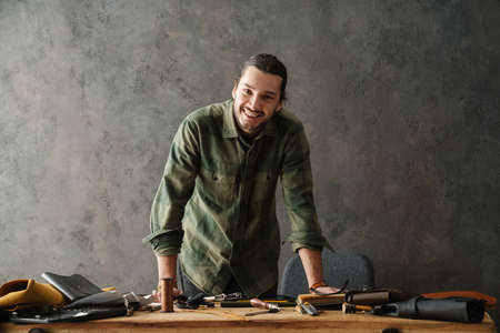 Smiling middle aged man leathersmith working at his workshop, standing at the table