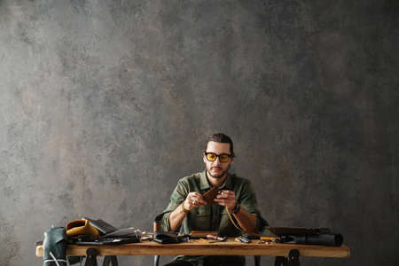 Bearded focused craftsman designing leather bag while working in workshop