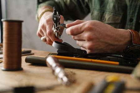 White craftsman using tool while working with leather in workshopの写真素材