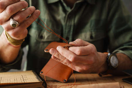 White craftsman sewing while making leather wallet in workshopの写真素材