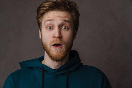 White ginger man with beard expressing surprise at camera isolated over grey background