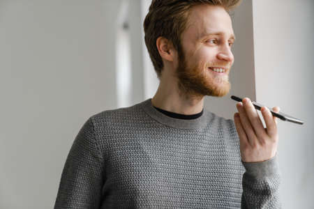 Ginger young man talking on mobile phone while standing indoors