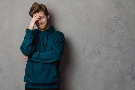 White ginger man with beard smiling and covering his face isolated over grey background