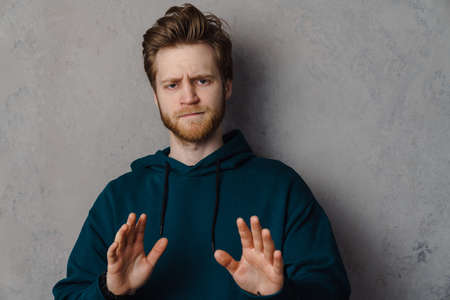White ginger man with beard frowning and showing stop gesture isolated over grey background