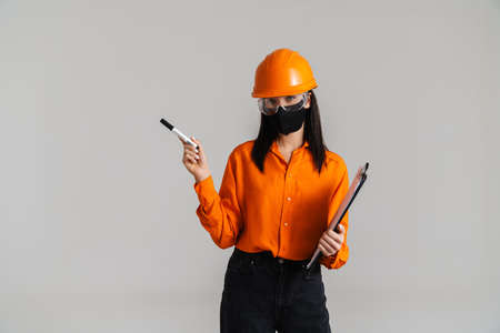 Young woman in safety glasses and face mask posing with clipboard isolated over grey backgroundの写真素材