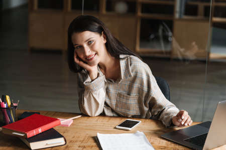Young brunette woman working with laptop while sitting at desk in office