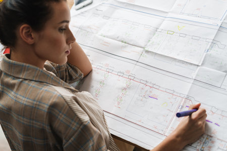Young brunette woman working with drawings while sitting at desk in officeの写真素材