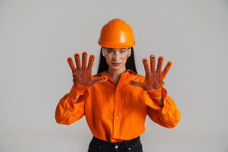 Young brunette woman in safety glasses and helmet showing her palms isolated over grey backgroundの写真素材
