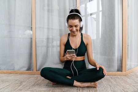 White woman listening music with headphones and cellphone while working out at homeの写真素材