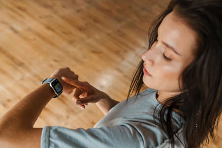 Young brunette white woman standing in the studio, resting after exercises, checking fitness watchの写真素材