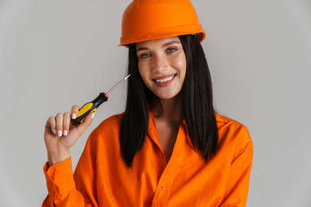 Young woman in helmet smiling while posing with screwdriver isolated over grey backgroundの写真素材