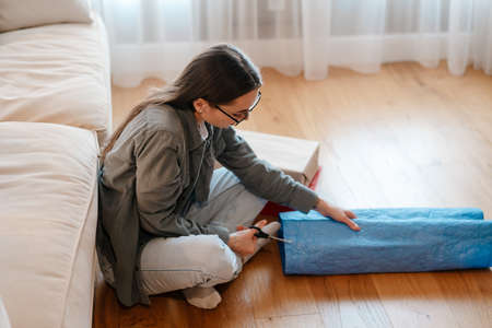White brunette woman wrapping presents while sitting on floor at home