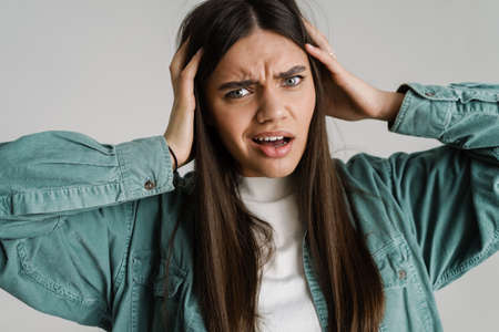 Young displeased woman looking at camera while holding her head isolated over white backgroundの写真素材