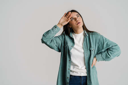 Young tired woman rubbing her forehead while looking upward isolated over white background