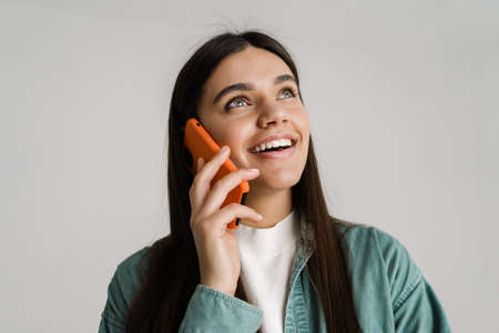 Young brunette woman smiling while talking on mobile phone isolated over white background