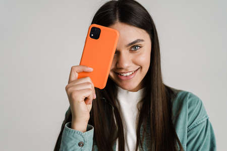 Young brunette woman smiling while posing with mobile phone isolated over white backgroundの写真素材