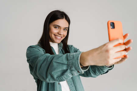 Young smiling woman taking selfie photo on mobile phone isolated over white backgroundの写真素材