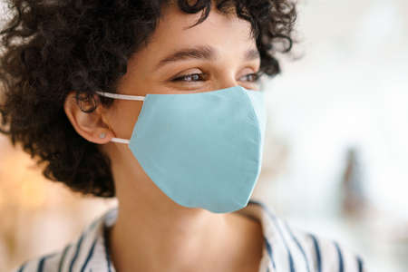 Beautiful curly happy woman in face mask posing indoorsの写真素材