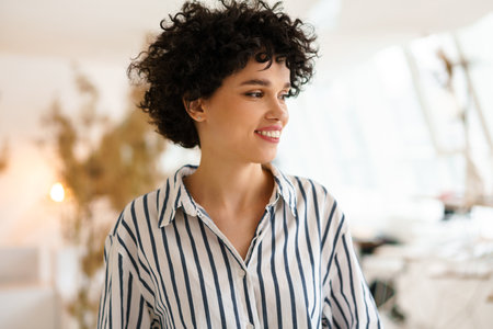 Beautiful curly happy woman smiling and looking aside indoorsの写真素材