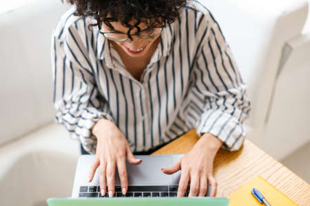 Beautiful happy woman in eyeglasses smiling while working with laptop in cafe