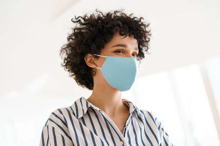 Beautiful curly happy woman in face mask posing indoorsの写真素材