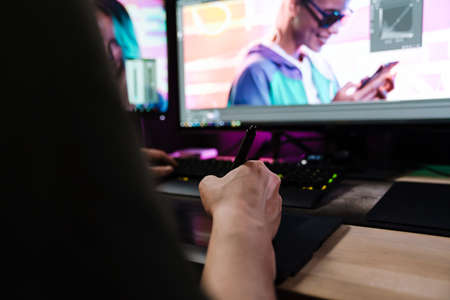 Back view of a young white man videographer working on a project with a touchpad on computer sitting...