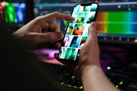 Close up of a white man hand holding mobile phone over computer screen on a table indoorsの写真素材