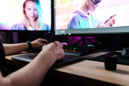 Back view of a young white man videographer working on a project with a touchpad on computer sitting at the desk indoorsの写真素材