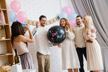 Young excited couple blowing up surprise balloon during gender reveal party indoorsの写真素材