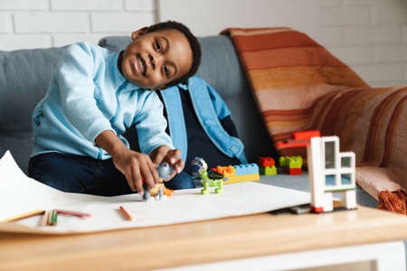 Black smiling boy paying with toys while sitting on sofa at homeの写真素材