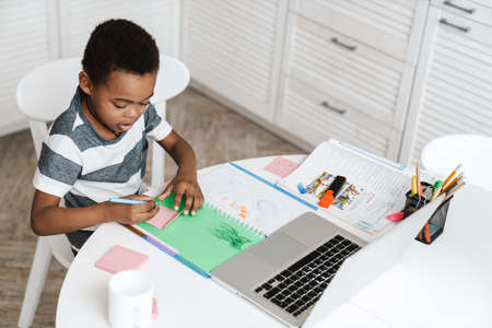 Black boy using laptop and drawing while sitting at homeの写真素材