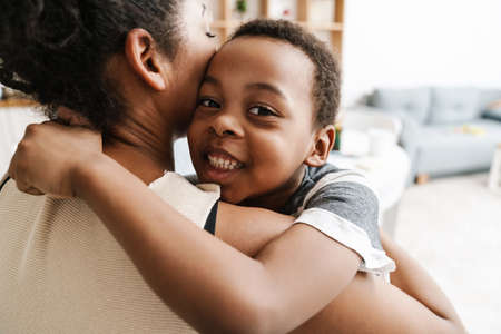Black elementary boy smiling while hugging her mother at home