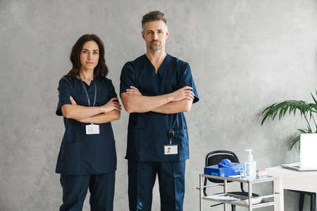 Two confident doctors in medical masks standing indoors, arms foldedの写真素材
