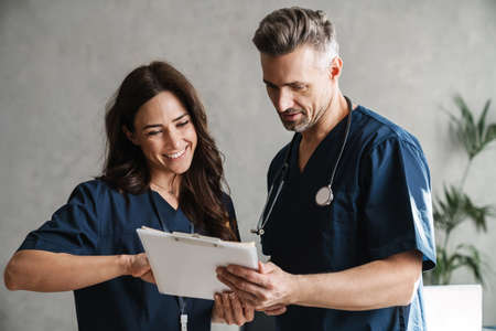 Two smiling doctors in medical uniforms discussing patient anamnesis together, considering test results indoorsの写真素材