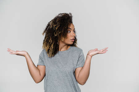 The surprised woman looking to the side and spreading her hands while standing in the light studioの写真素材