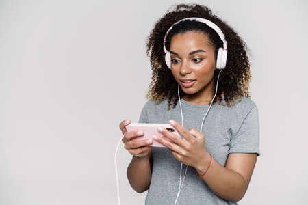 A portrait of a pensive woman in headphones holding a phone in her hands while standing in the light studioの写真素材