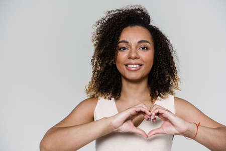 The smiling woman showing heart gesture by joining two hands while standing in the light studioの写真素材