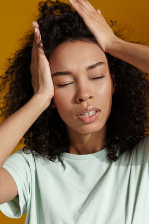Young african woman wearing t-shirt posing and holding her head isolated over brown wall