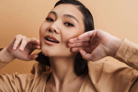 Young asian brunette woman posing and looking at camera isolated over beige backgroundの写真素材
