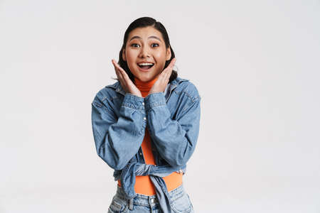 Happy smiling young asian brunette woman in denim jacket posing standing over gray backgroundの写真素材