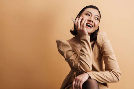 Young asian woman smiling while posing with eyelash curler isolated over beige background