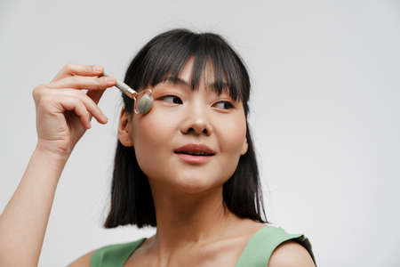 Young asian woman with piercing massaging face with jade roller isolated over white backgroundの写真素材